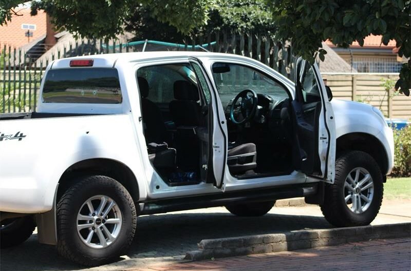 A white Isuzu bakkie riddled with bullet holes stands in a driveway of a residential area