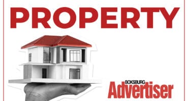 Black and white image of a hand holding a model of a house with a red roof with the word Property in red and the Boksburg Advertiser logo.