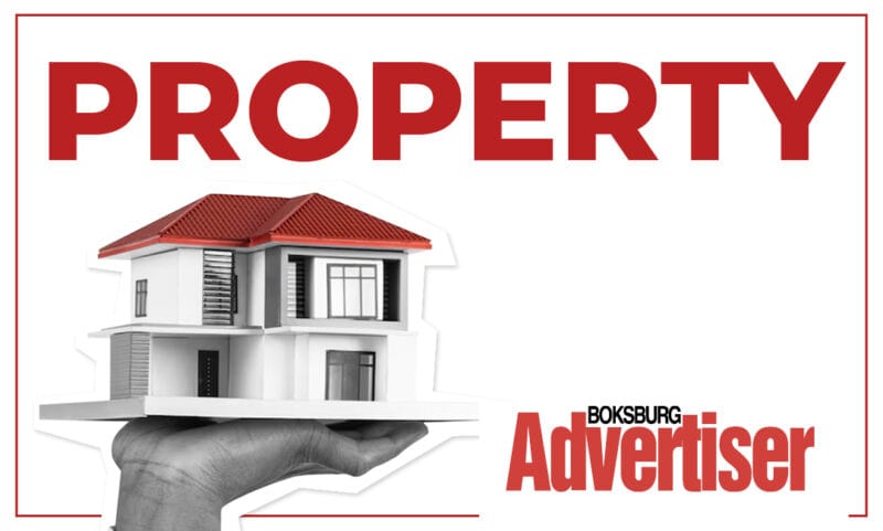 Black and white image of a hand holding a model of a house with a red roof with the word Property in red and the Boksburg Advertiser logo.