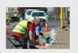 A man and woman painting the kerbsides of the raised island at the intersection of roads.