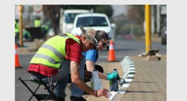 A man and woman painting the kerbsides of the raised island at the intersection of roads.