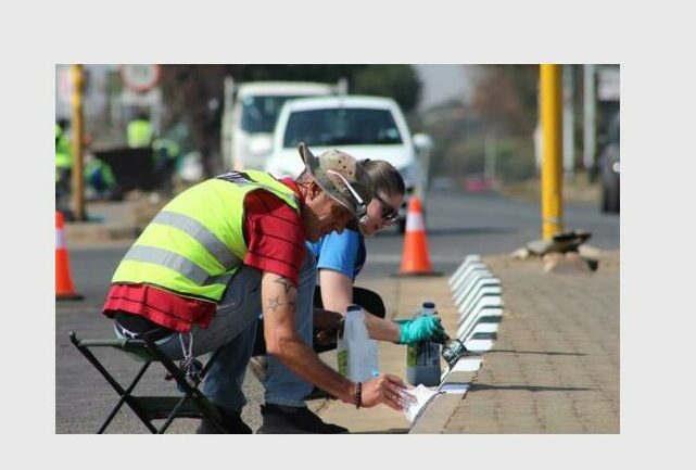 A man and woman painting the kerbsides of the raised island at the intersection of roads.