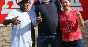 Two men and a woman posing for a photo with a company logo in the background