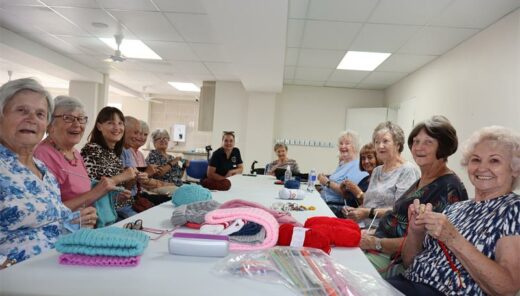 a group of elderly people sitting a round a table and knitting