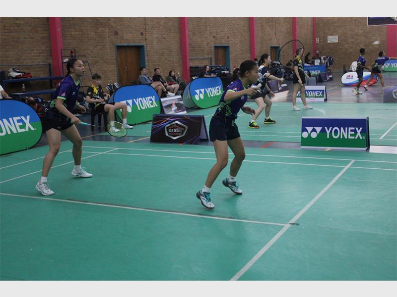 Two female badminton players in action on an indoor court. 