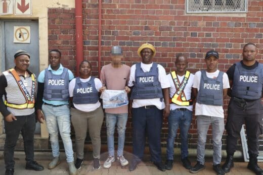A group of police officers and a suspect holding a plastic bag carrying a gun