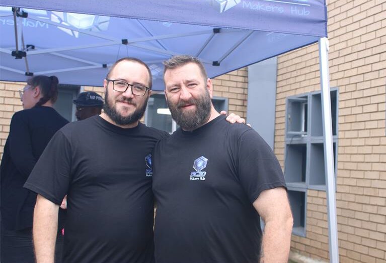 Two men in black t-shirts standing under a gazebo next to a building