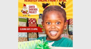 A poster promoting Santa Shoebox Project depicting a yellow sunrise in the background, red text and a smiling black girl with two pigtails.