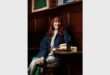 A red-haired woman dressed in light clothing and a denim jackets sitting at a small wooden table in a pub with a crisp sandwich and block of Kerrygold butter next to her.