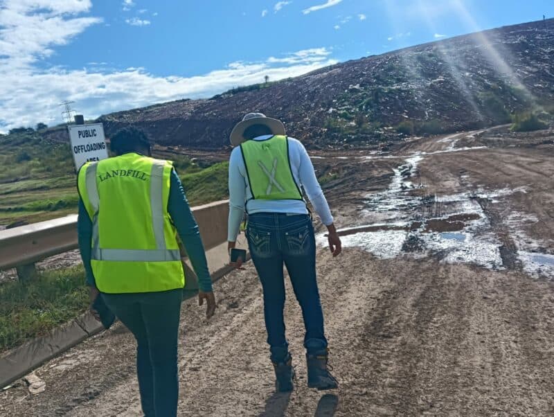 Two workers , a man and a woman in reflective safety clothing, walking towards a landfil site