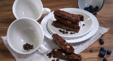 A display of empty white coffee cups and white plates with chocolate biscuits on them.