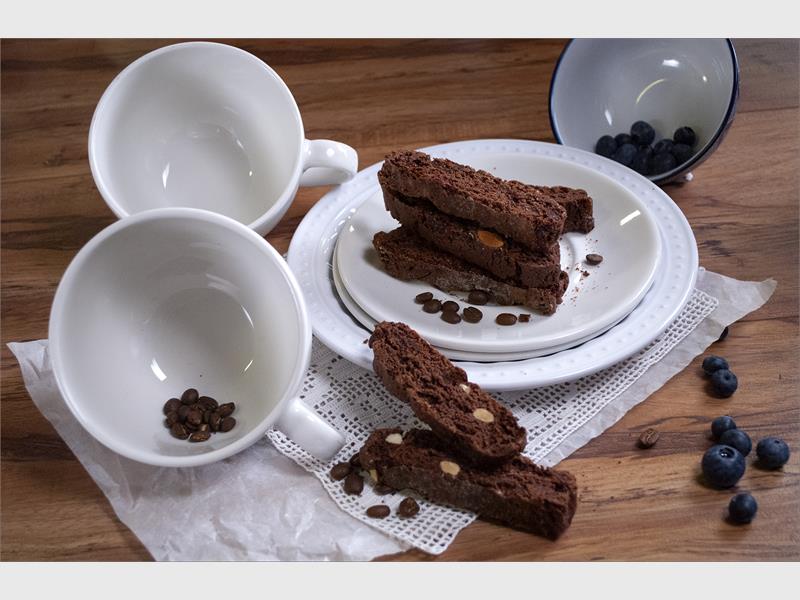 A display of empty white coffee cups and white plates with chocolate biscuits on them.