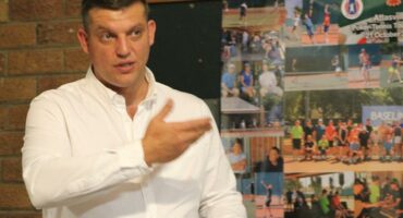 a man in a white shirt holding a white paper and gesturing while addressing a crowd