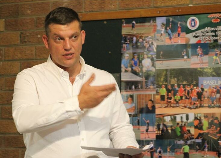 a man in a white shirt holding a white paper and gesturing while addressing a crowd