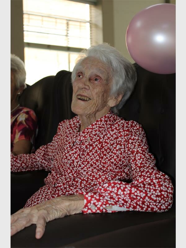 An old woman laughing as she sits in a chair wearing a red and white dress.