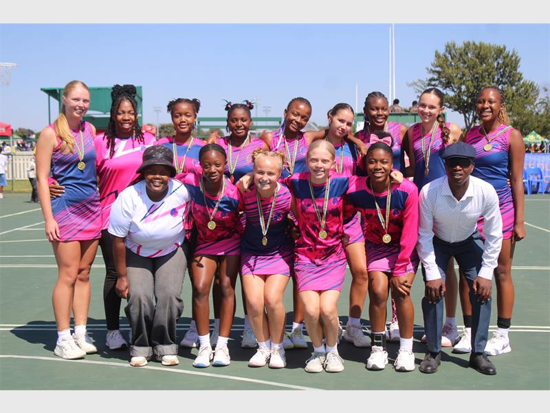 A netball team in their pink and blue kit, standing in two rows with their coaches.