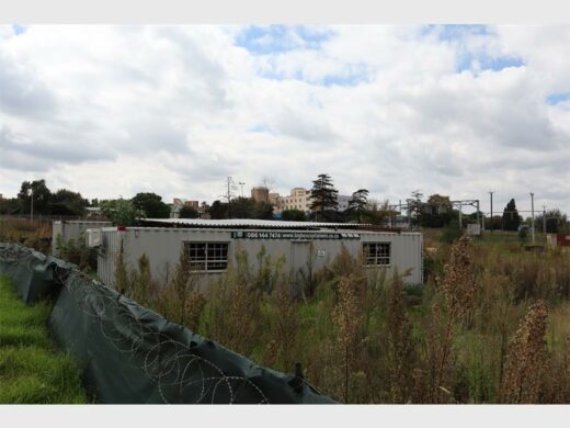 a construction site with container offices in an overgrown veld