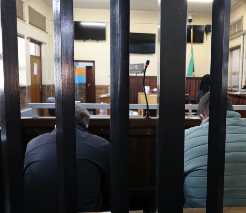 Two men sit side by side in the court dock during proceedings at the Boksburg Magistrate’s Court, as their bail application is heard.