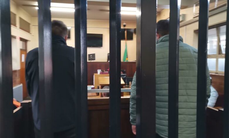 Two men photographed from the back behind bars in a courtroom.
