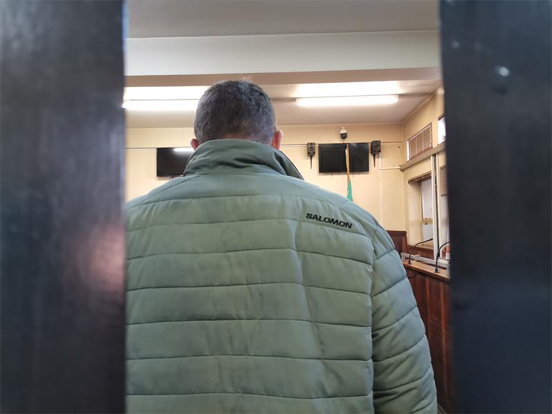 A man photographed from behind wearing a green jacket while walking into a courtroom.