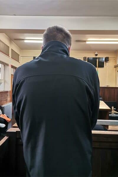 A man wearing a dark jacket photographed from behind in the dock of a courtroom.