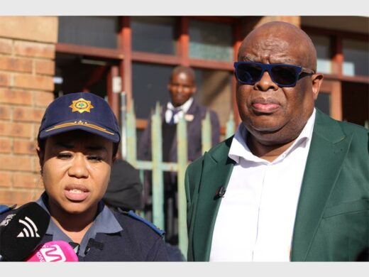 a police woman IN UNIFORM STANDING NEXT TO A MAN WEARING GLASSES AND A GREEN AND WHITE TOP