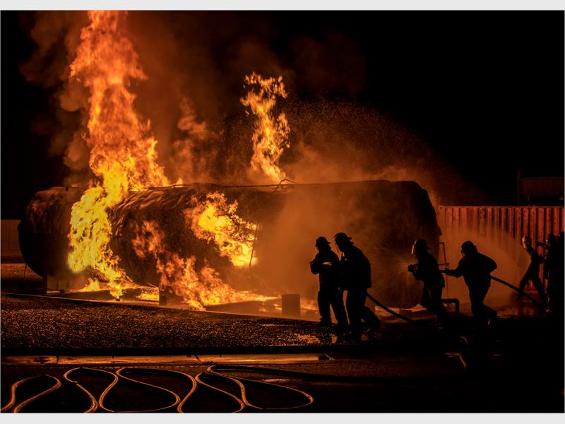 A raging fire with four firefighters to the right of the photo.