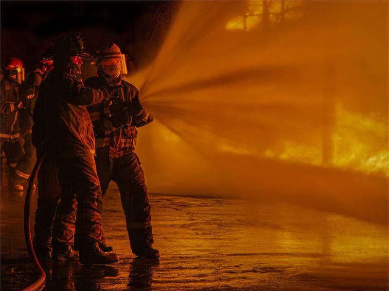 Two firefighters holding a hose spraying a strong stream of water towards a fire.