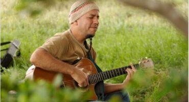 man playing guitar in an overgrown field