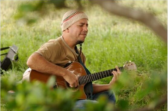 man playing guitar in an overgrown field