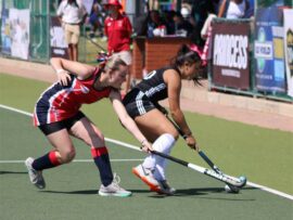 A hockey match in action with two players reaching with their sticks towards the ball.