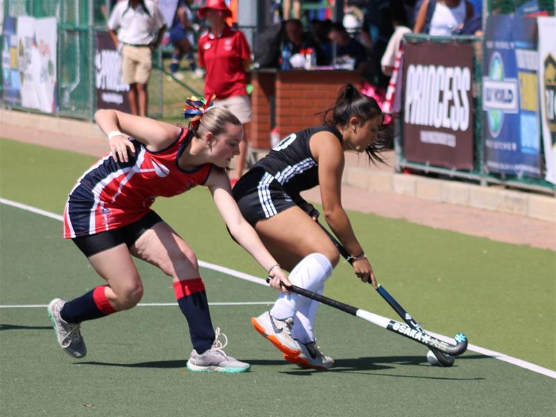 A hockey match in action with two players reaching with their sticks towards the ball.