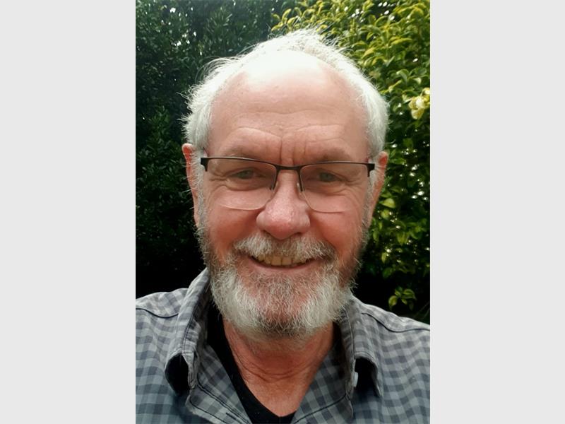 A smiling man with grey hair, moustache and hair, wearing glasses and a checked shirt.