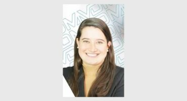 A smiling white woman with long dark hair over her shoulders wearing a dark jacket.