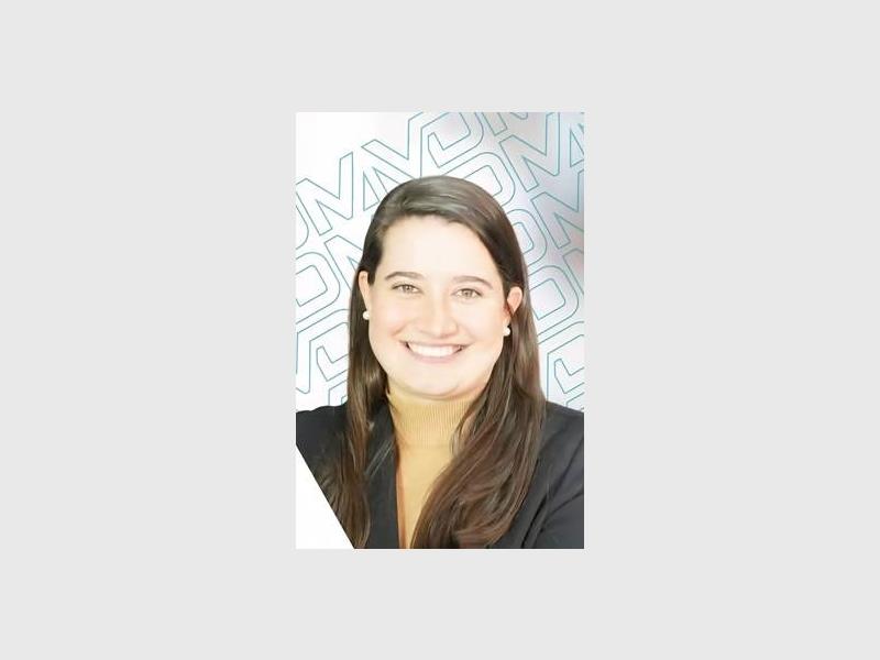 A smiling white woman with long dark hair over her shoulders wearing a dark jacket.