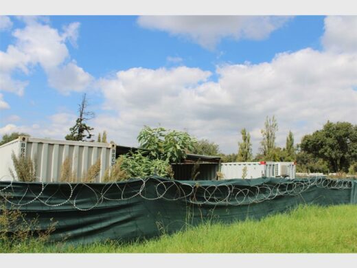 a construction site with container offices in an overgrown veld