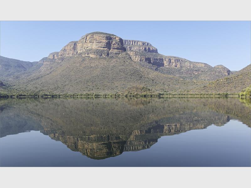 A photo of a mountain next to a river with its reflection in the water. 
