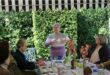 Gray haired woman gestures with her hands as she speaks to a group of women