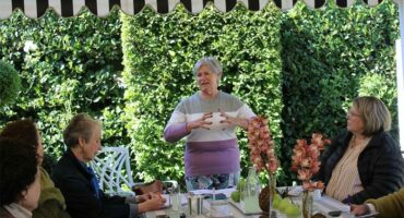 Gray haired woman gestures with her hands as she speaks to a group of women