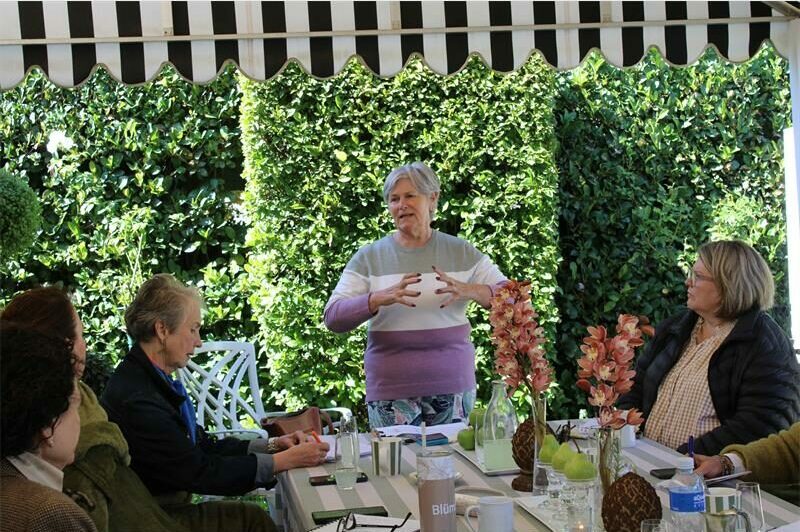 Gray haired woman gestures with her hands as she speaks to a group of women