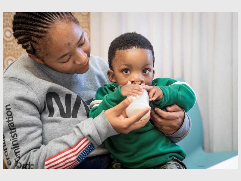 A mom with a toddler on her lap feeding the child a bottle.