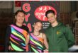 A male and female gymnast in brightly coloured shirts with their coach wearing a springbok jacket.