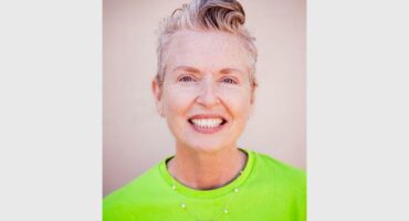 A head and shoulders photo of a smiling woman with blonde hair wearing a bright green shirt.