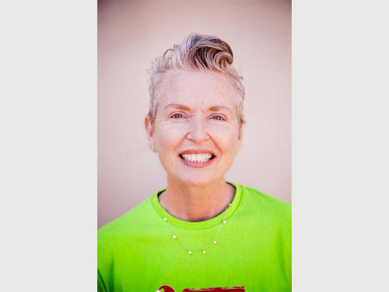A head and shoulders photo of a smiling woman with blonde hair wearing a bright green shirt.