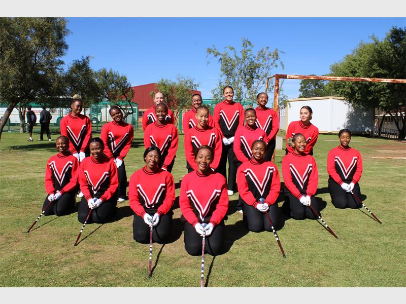 A squad of drum majorettes posing for a photo in red shirts and black pants with white gloves and batons outstretched. 