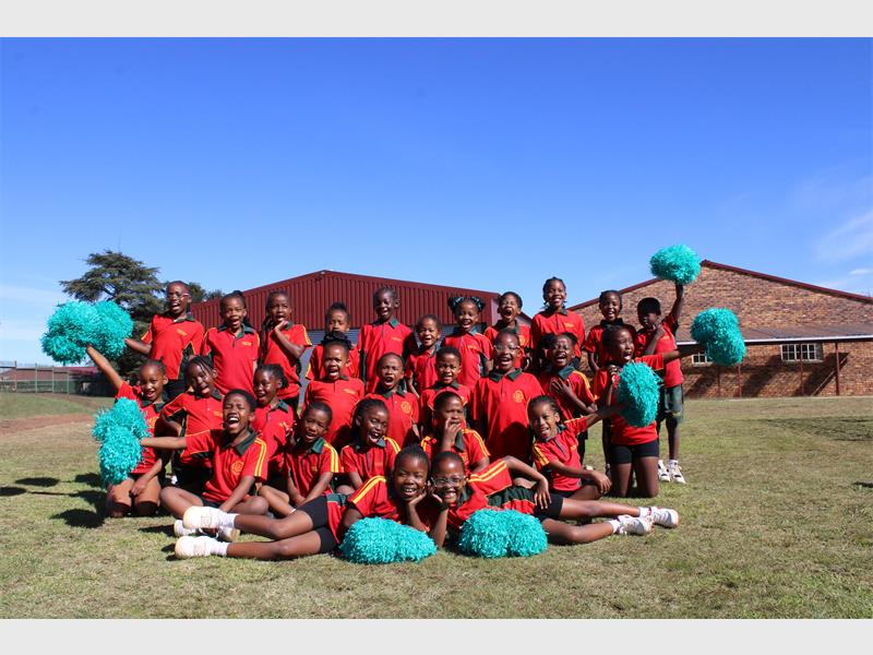 A squad of drum majorettes posing for a photo with red kit on and turquoise pom poms. 