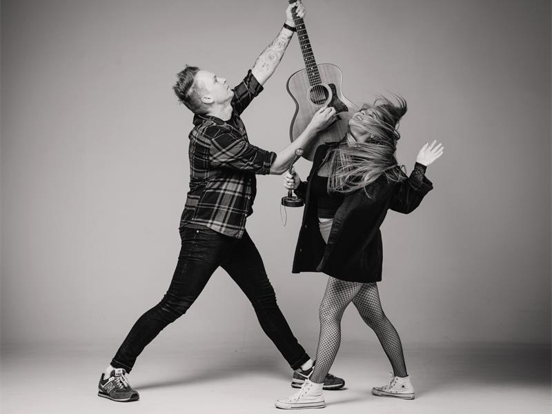 A black and white image of a man and a woman dancing and reaching up towards a guitar she is holding.