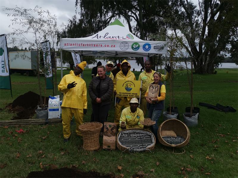 Seven people at Homestead Dam with a white gazebo in the background posing with bags of soil for planting trees. 