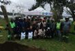 A big group of people posing with bags of soil for tree planting at Homestead Dam with a white gazebo in the background.