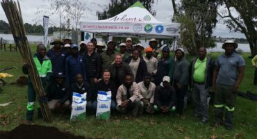 A big group of people posing with bags of soil for tree planting at Homestead Dam with a white gazebo in the background.